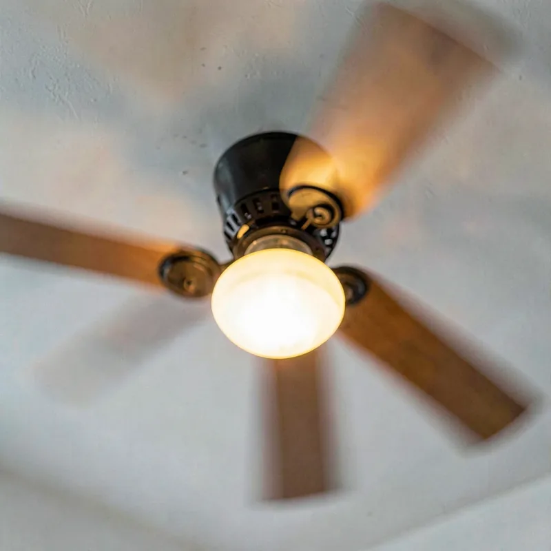 Close view from below of a ceiling fan light fixture glowing warm against a white ceiling