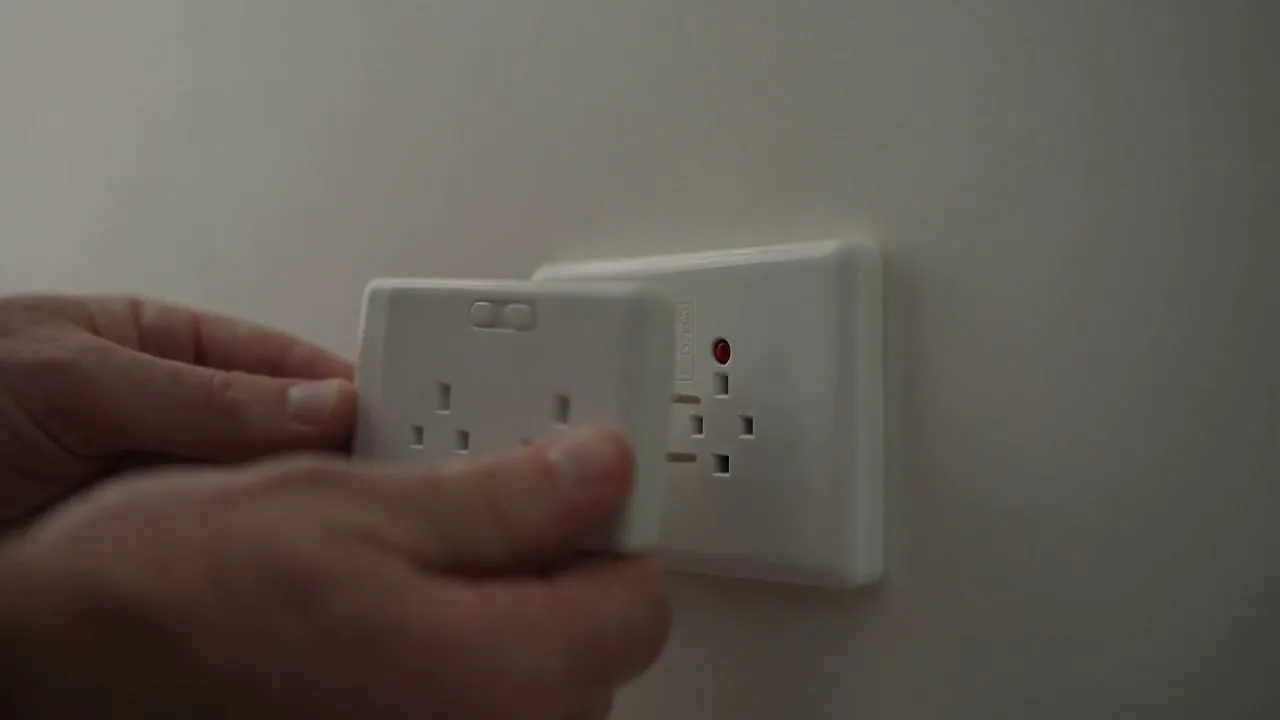 A hand testing a newly installed white power point on the wall